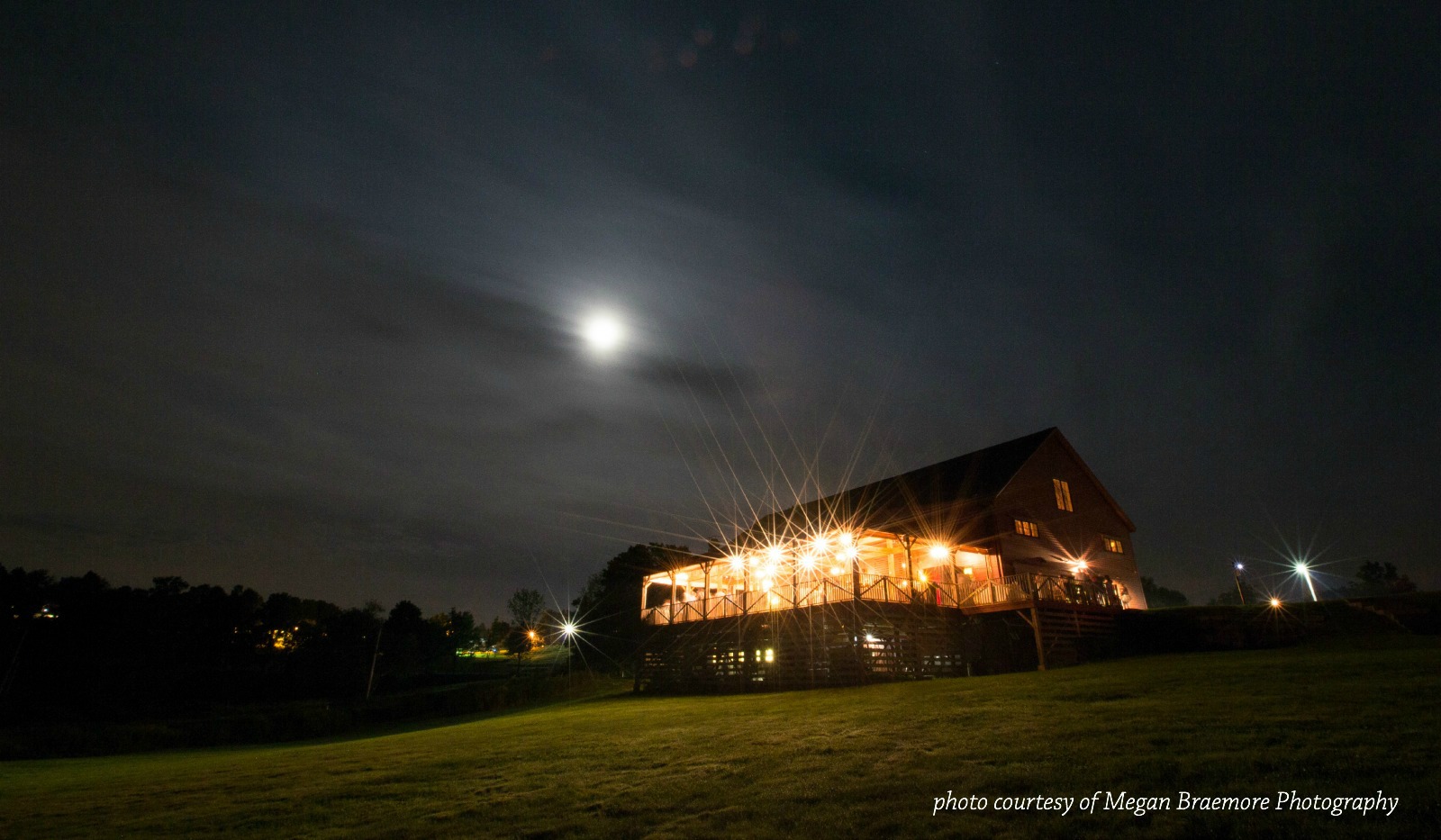 View of barn fully lit in the evening, with full moo in background 