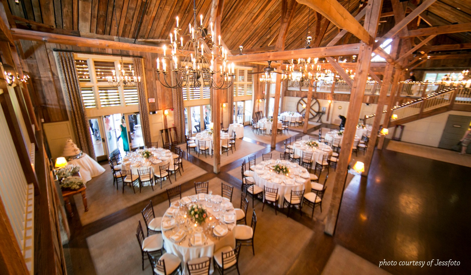 Barn interior fully set for event with several large rounds set for 10 guests each, vaulted ceilings and elegant chandeliers 